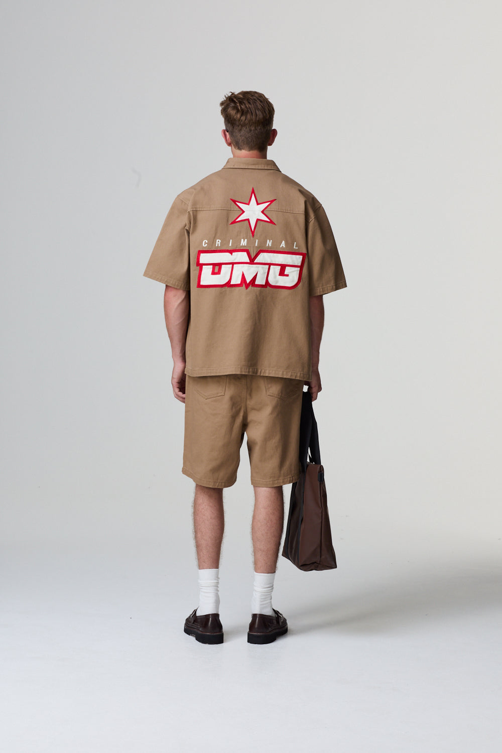 Model wearing a beige Criminal Damage shirt and shorts against a grey background