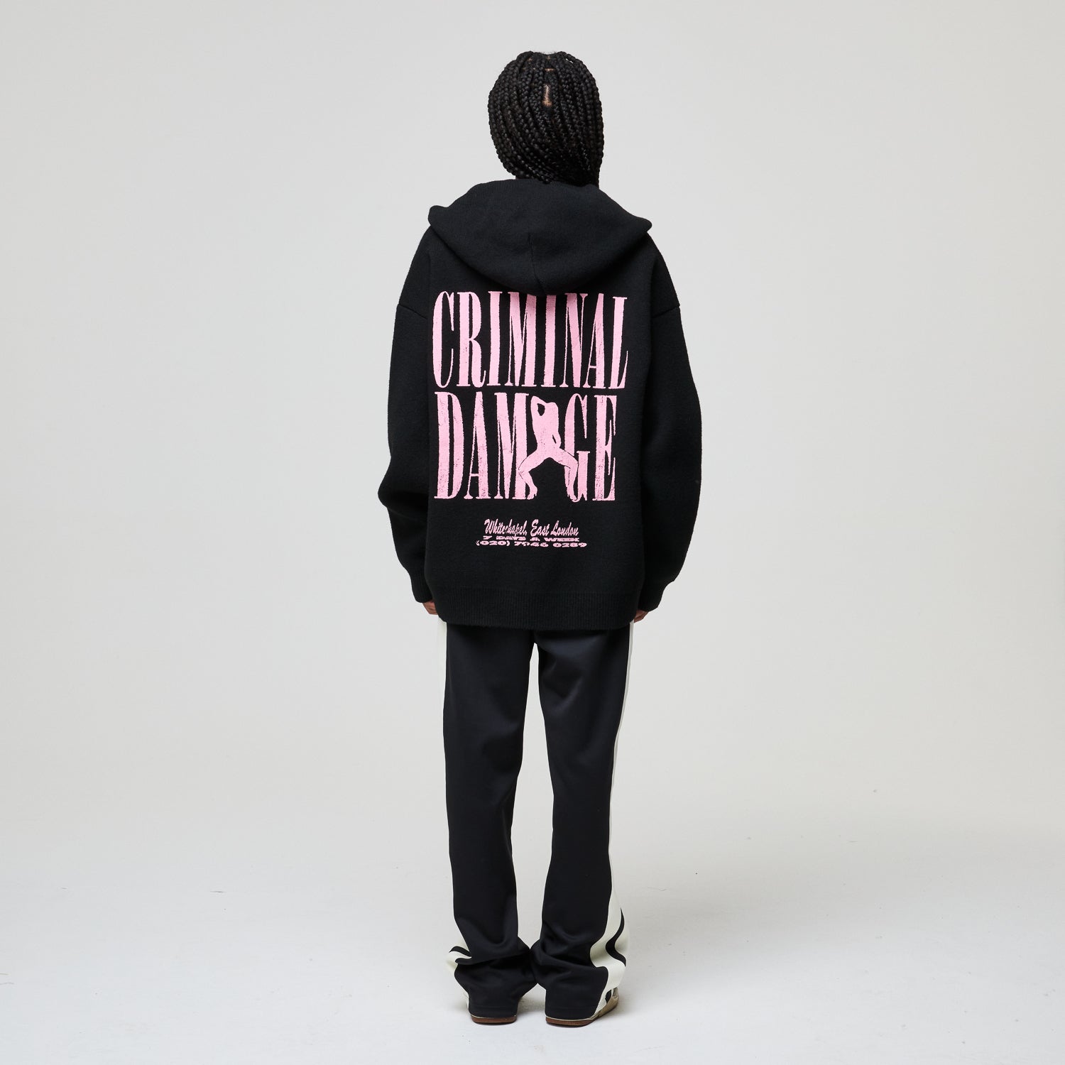 Person wearing a black hoodie with pink text on the back against a white background