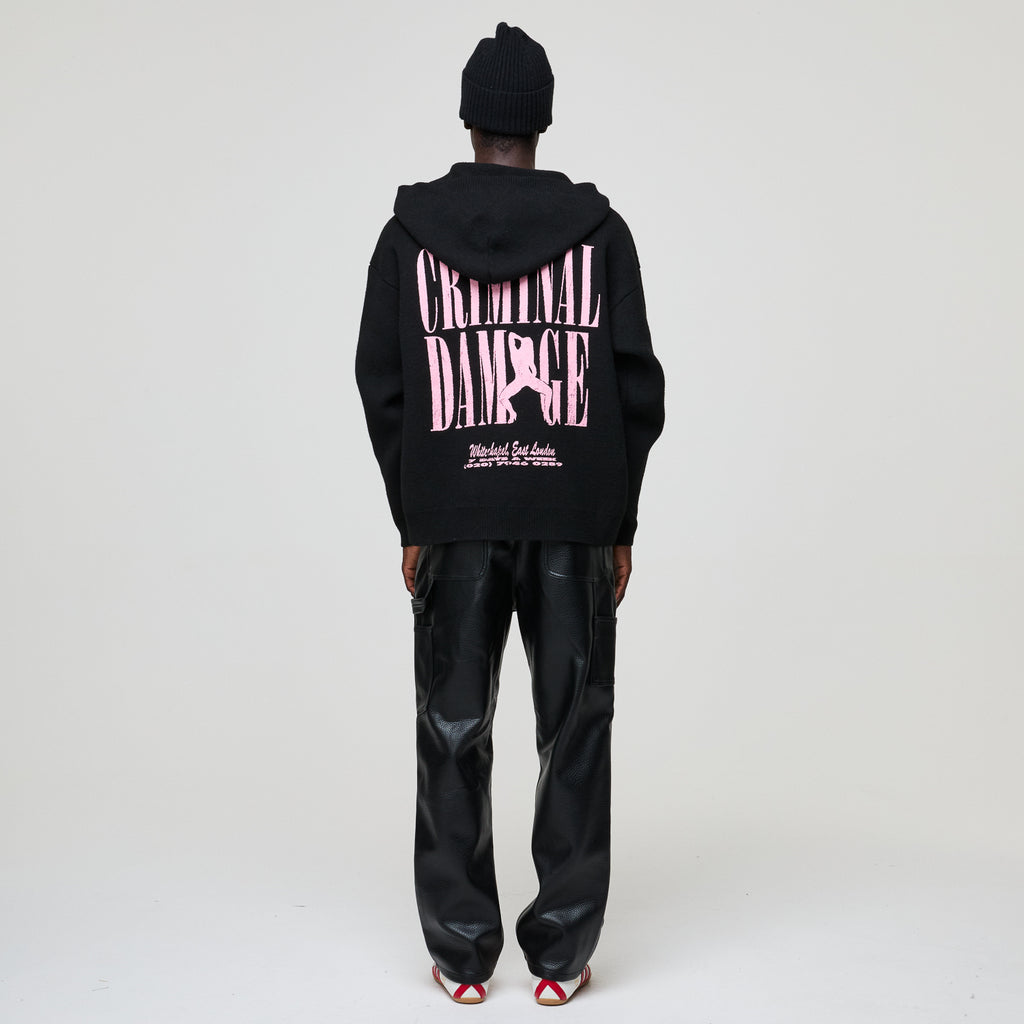 Person wearing a black hoodie with 'Criminal Damage' text on the back, standing against a white background.
