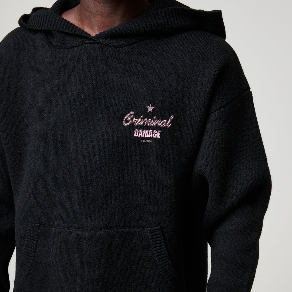Black hoodie with 'Criminal Damage' embroidery on a neutral background
