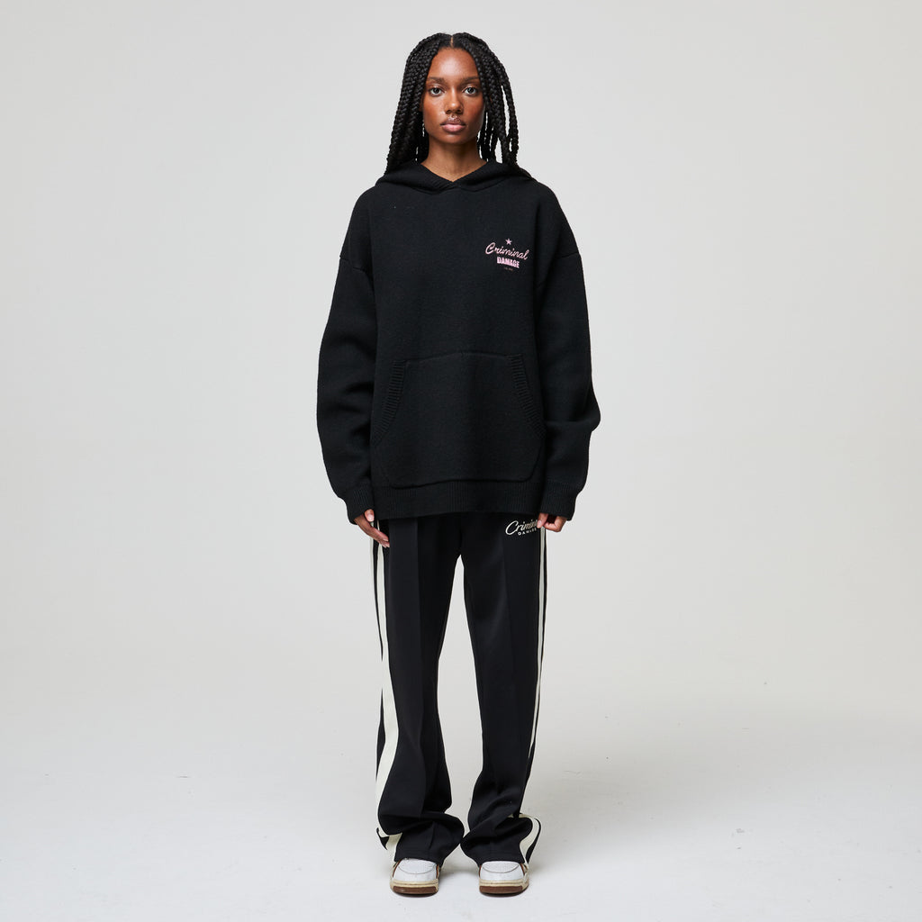 Person wearing a black hoodie and tracksuit with visible branding on a white background