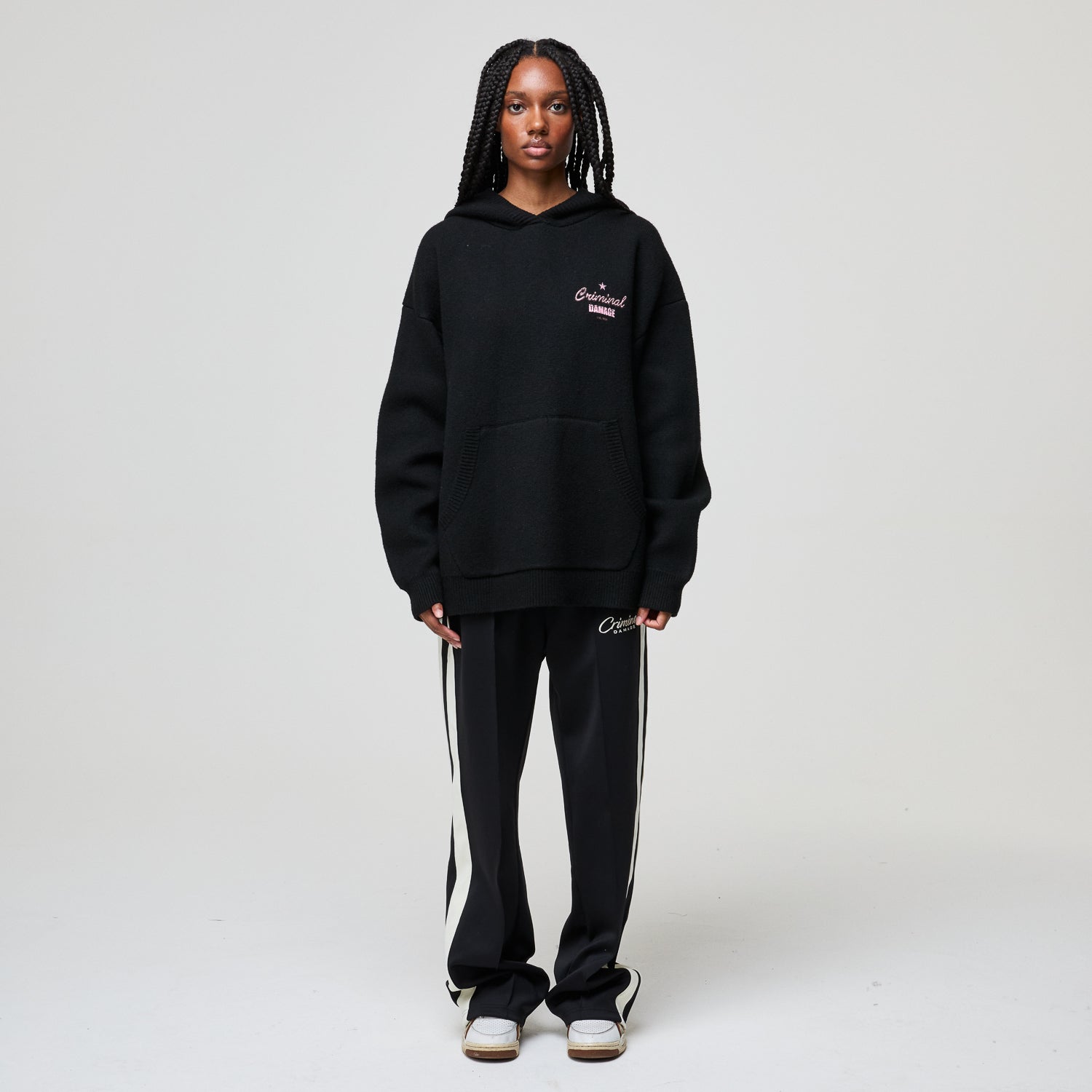 Person wearing a black hoodie and tracksuit with visible branding on a white background
