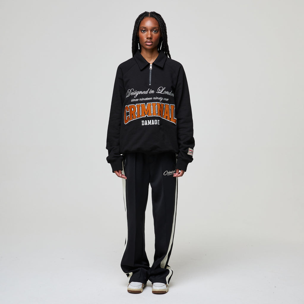 Person wearing a black Criminal Damage tracksuit with visible branding on a white background