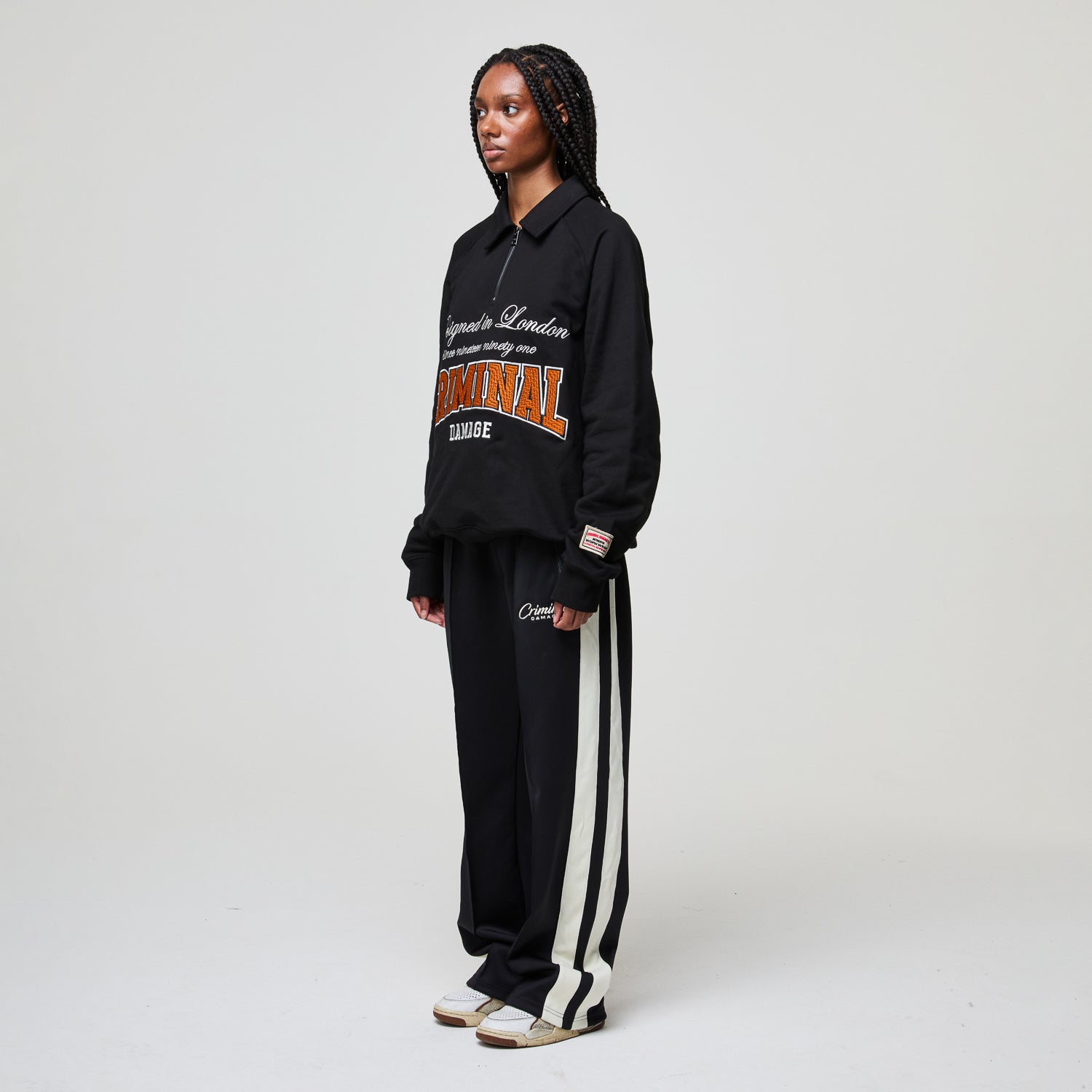 Person wearing a black Criminal Damage tracksuit with 'Lonsdale London' branding on a white background