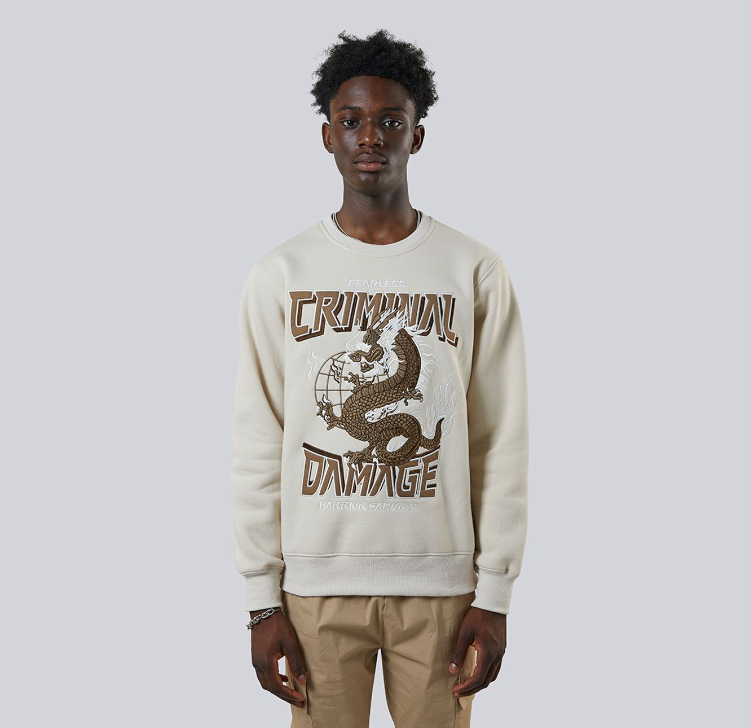 Person wearing a cream sweatshirt with 'Criminal Damage' graphic design on a plain background