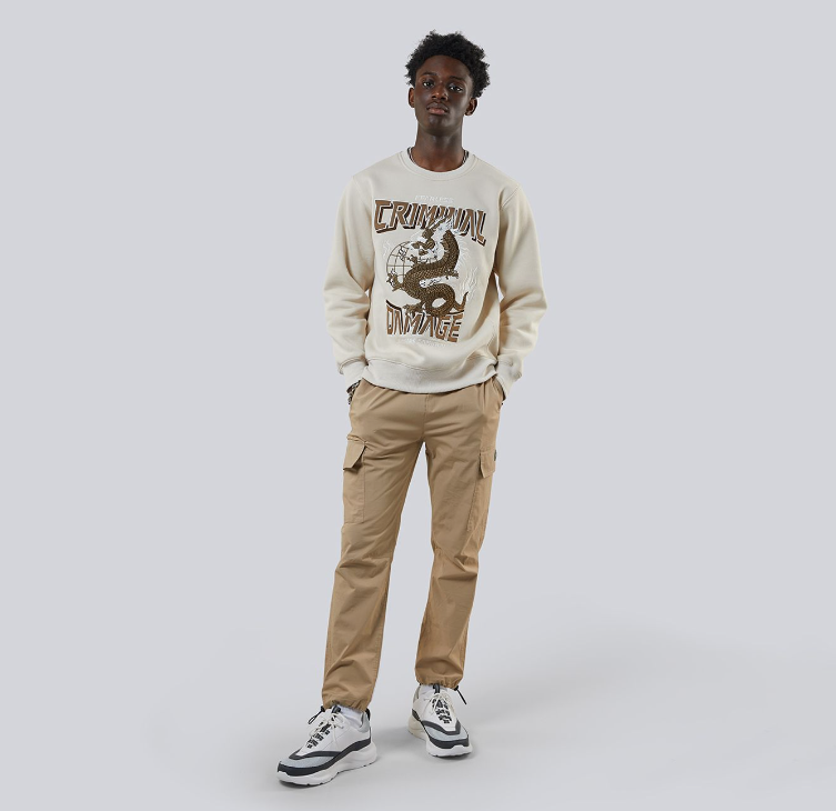 Man wearing a beige sweatshirt with graphic design and beige pants on a white background