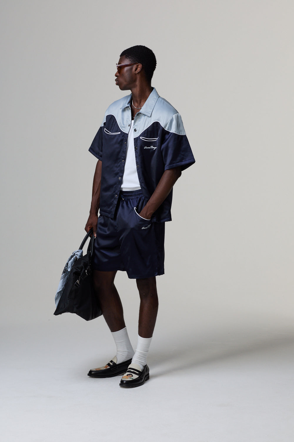 Model wearing a Criminal Damage navy and white outfit with a bag on a grey background