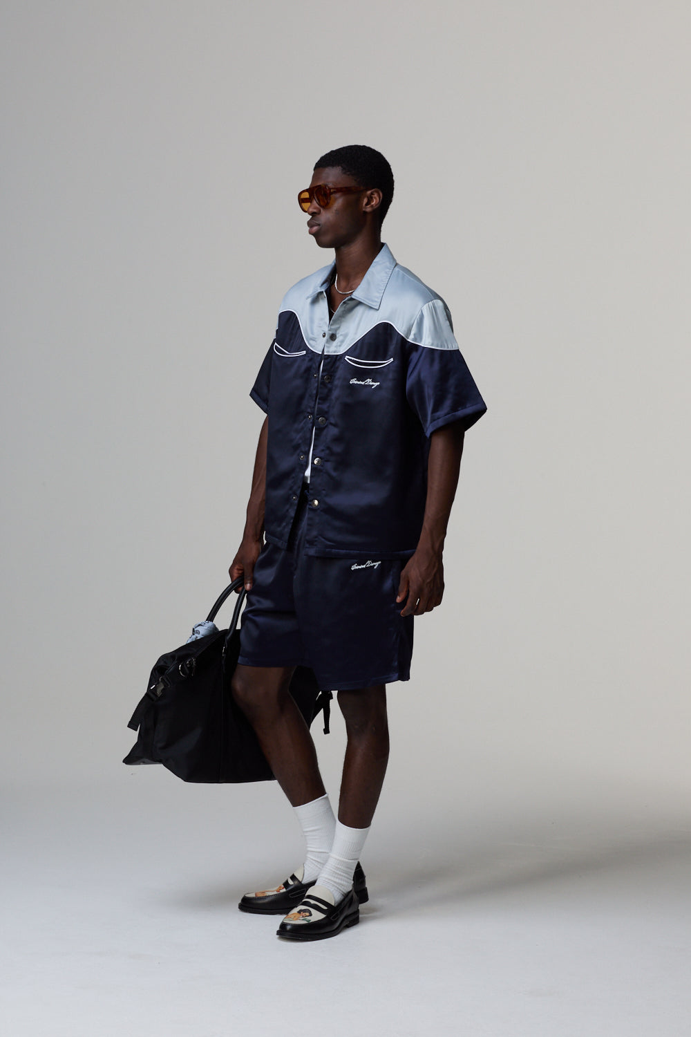 Model wearing a Criminal Damage navy and white outfit with a black bag on a grey background