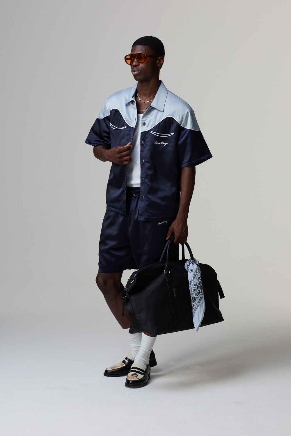 Model wearing a Criminal Damage navy and white outfit with a black bag on a grey background