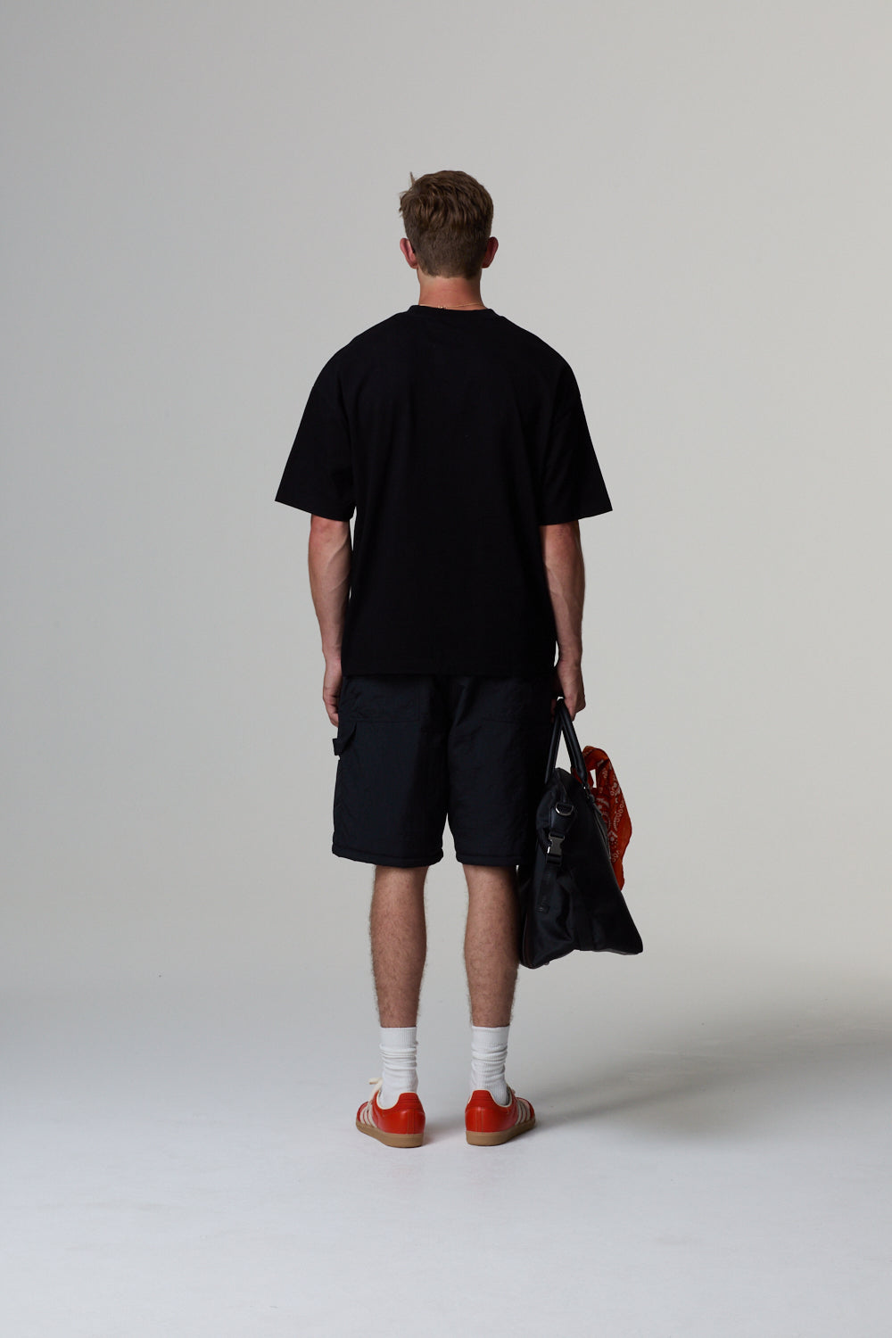 Model wearing a Criminal Damage black t-shirt and shorts holding a black bag on a grey background